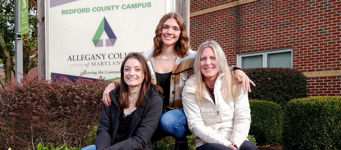 Students sitting infront of the College Sign